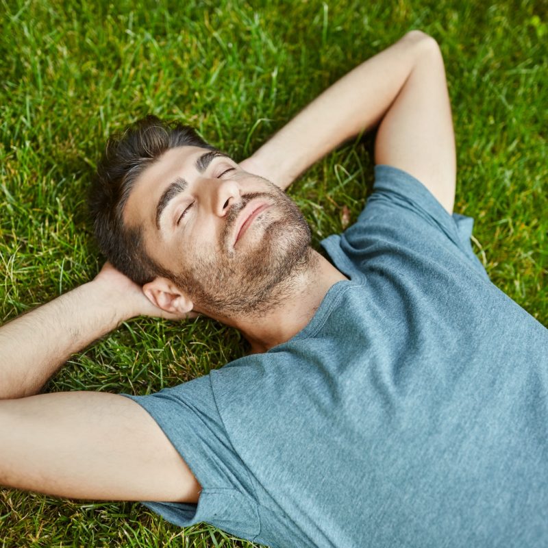 Portrait of young mature good-looking caucasian man in blue shirt peaceful lying on grass with yes